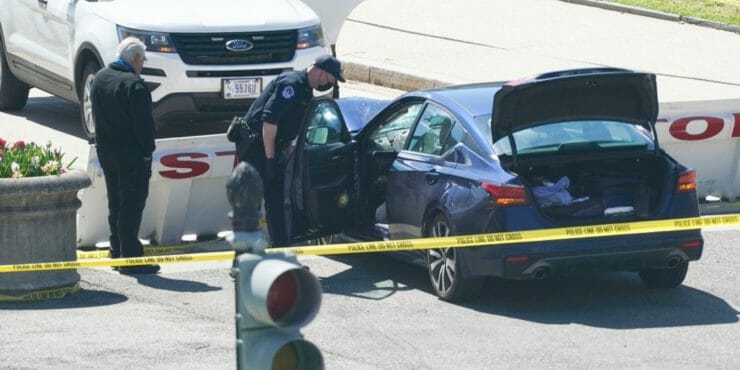 Policajti stoja neďaleko automobilu, ktorý narazil do bariéry pred sídlom vlády USA v Capitol Hill vo Washingtone v piatok 2. apríla 2021.