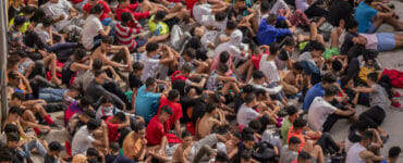 Maloletí migranti bez sprievodu sedia pred skladom používaným ako dočasný prístrešok v španielskej enkláve Ceuta.