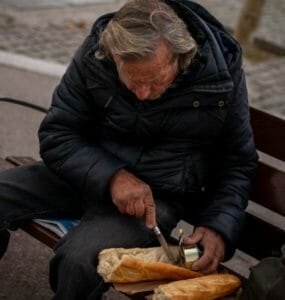 Bezdomovec si pripravuje sendvič k obedu v parku.