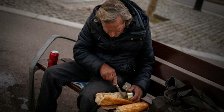 Bezdomovec si pripravuje sendvič k obedu v parku.