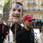 Demonštrant drží masku s podobizňou Macrona.