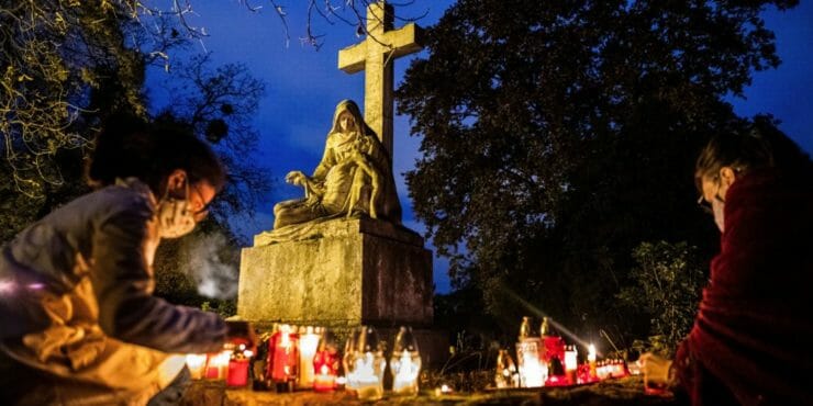 Ľudia s ochrannými rúškami zapaľujú sviečky na cintoríne.