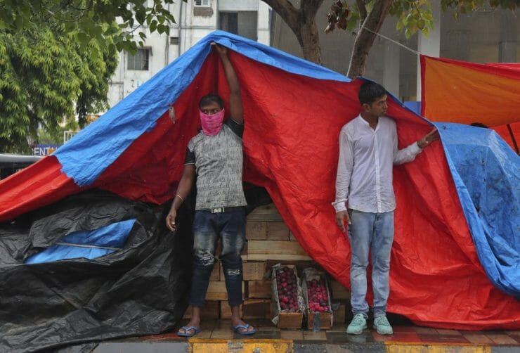 Indickí pouliční predavači ovocia sa skryli pod plachtu pred monzúnovým dažďom.