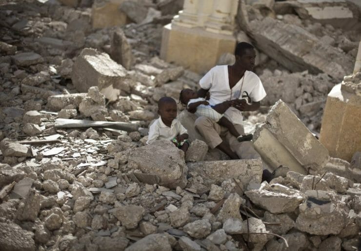 Muž s dvoma deťmi sedí v ruinách katedrály počas svätej omše v haitskej metropole Port-au-Prince 12. januára 2011.