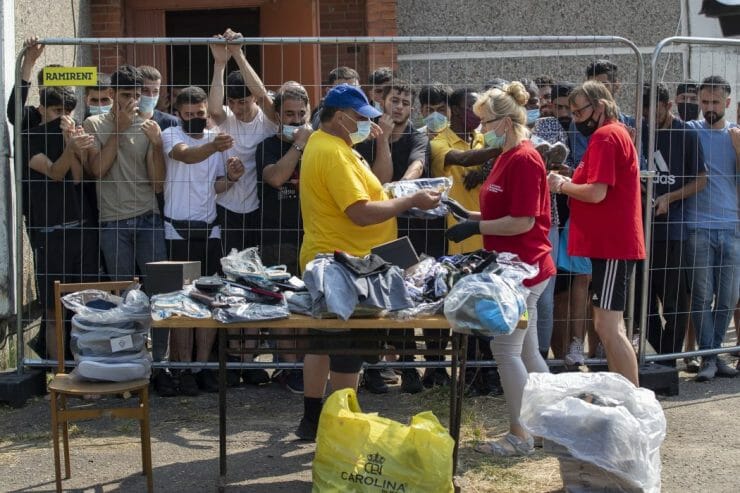 Litovčania rozdávajú veci migrantom, ktorí stoja za plotom v utečeneckom tábore v litovskej dedine Verebiejai 11. júla 2021.