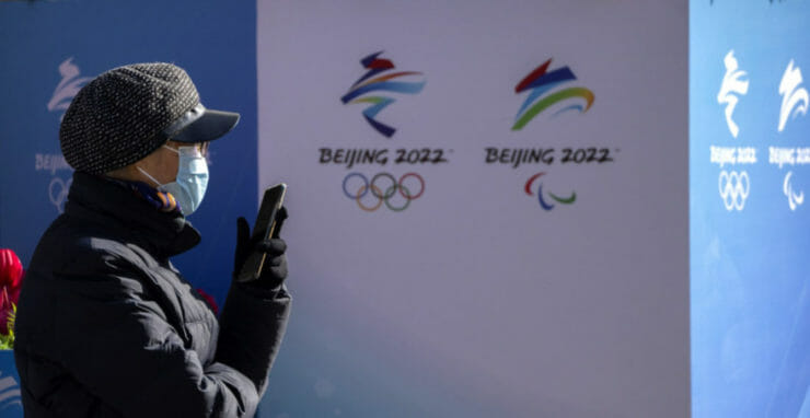 Žena s rúškom kráča okolo logo blížiacich sa zimných olympijských a paralympijskych hier v Pekingu.