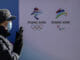 Žena s rúškom kráča okolo logo blížiacich sa zimných olympijských a paralympijskych hier v Pekingu.