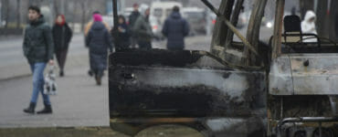 Ľudia kráčajú okolo zhoreného autobusu po nepokojoch v kazašskej Alma-Ate v utorok 11. januára 2022.