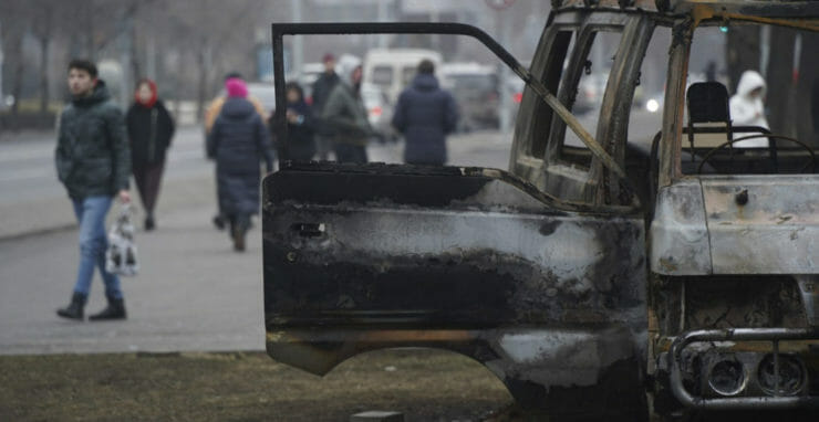 Ľudia kráčajú okolo zhoreného autobusu po nepokojoch v kazašskej Alma-Ate v utorok 11. januára 2022.