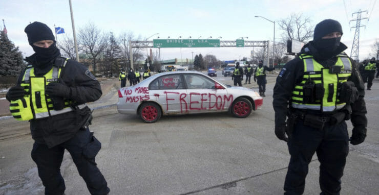 Policajti stoja počas demonštrácie proti pandemickým opatreniam na moste vedúcim do Spojených štátov