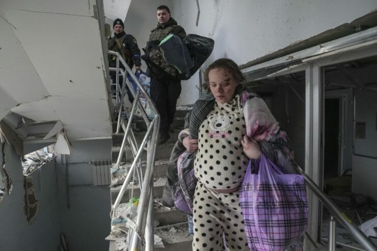 Zranená tehotná žena kráča po schodoch v zničenej budove pôrodnice po ostreľovaní v Mariupole.