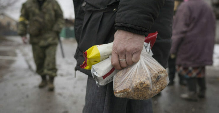Na ilustračnej snímke muž drží v ruke potraviny na ulici po ruskom leteckom útoku v Gorenke, na predmestí Kyjeva 2. marca 2022.