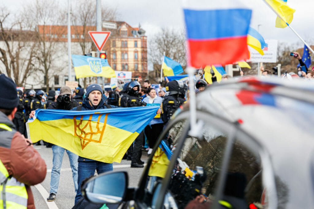 Antiruský demonštrant drží ukrajinský vlajku pred autom, ktoré je súčasťou dlhého proruského konvoja v nemeckom meste Hannover v nedeľu 10. apríla 2022.