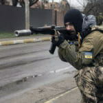 Na ilustračnej snímke ukrajinský vojak zabezpečuje presun spolubojovníkov počas kontroly nástražných pásc v meste Buča pri Kyjeve.