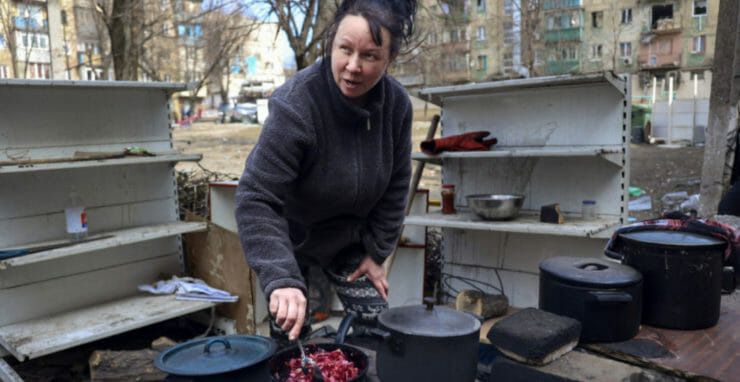 Na ilustračnej snímke žena varí na dvore poškodených bytoviek po ostreľovaní na okraji ukrajinského Mariupolu.