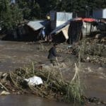 Muž sa brodí cez rieku v osade počas ničivých záplav v juhoafrickom meste Durban vo štvrtok 14. apríla 2022.
