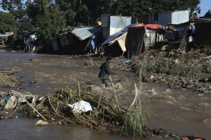 Muž sa brodí cez rieku v osade počas ničivých záplav v juhoafrickom meste Durban vo štvrtok 14. apríla 2022.