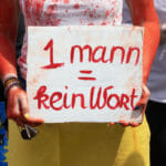 Žena v tričku pomaľovanom farbou tak, že to pripomínalo krv, drží transparent s nápisom Jeden muž = žiadne slovo počas demonštrácie v rámci Konferencie nemeckých katolíkov v juhozápadnom meste Stuttgart v piatok 27. mája 2022.