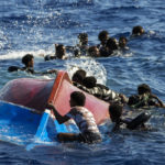 Skupina afrických migrantov pláva pri prevrátenej drevenej loďke, ilustračná snímka.