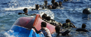 Skupina afrických migrantov pláva pri prevrátenej drevenej loďke, ilustračná snímka.