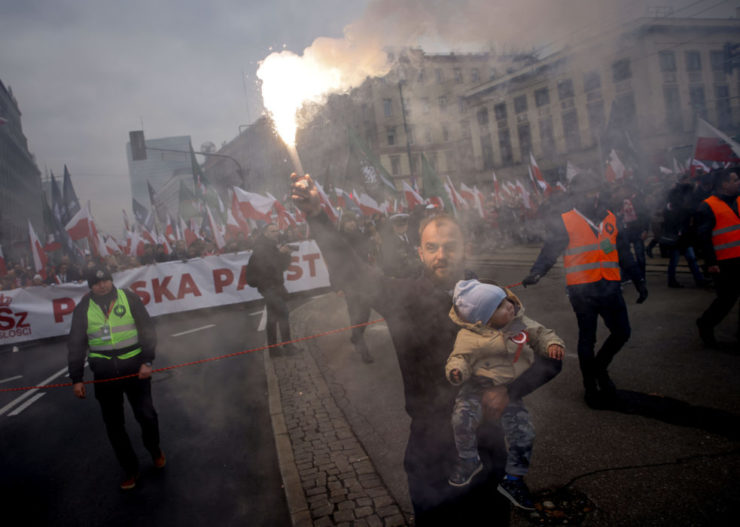 Muž drží dieťa a máva so svetlicou počas pochodu pri príležitosti Dňa nezávislosti v poľskom hlavnom meste Varšava v piatok 11. novembra 2022.