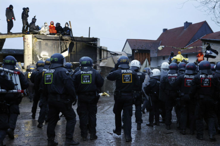 Policajti stoja pred barikádov klimatických aktivistov počas druhého dňa ich vysťahovania v dedine Lützerath.